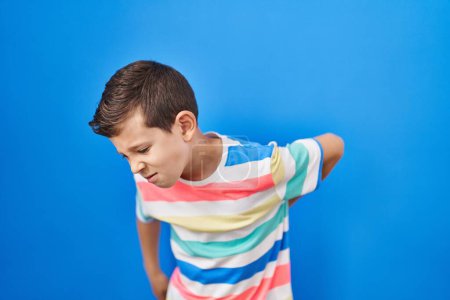 Photo for Young caucasian kid standing over blue background suffering of backache, touching back with hand, muscular pain - Royalty Free Image