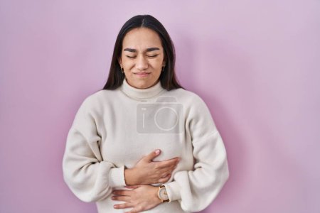 Téléchargez les photos : Jeune femme sud-asiatique debout sur fond rose avec la main sur le ventre parce que l'indigestion, la maladie douloureuse se sent mal. concept de douleur. - en image libre de droit
