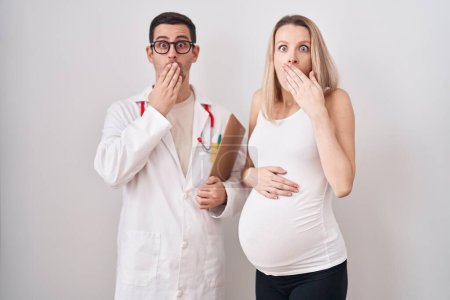 Téléchargez les photos : Jeune femme qui attend un bébé avec un médecin couvrant la bouche avec la main, choquée et effrayée par l'erreur. expression surprise - en image libre de droit