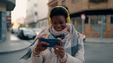 Foto de Joven mujer afroamericana sonriendo confiada jugando videojuego en la calle - Imagen libre de derechos