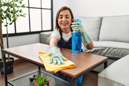 Foto de Mujer hispana de mediana edad trabajando como ama de llaves limpiando mesa en casa - Imagen libre de derechos