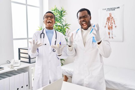 Foto de Jóvenes médicos afroamericanos que trabajan en una clínica médica celebrando locos y locos por el éxito con los brazos levantados y los ojos cerrados gritando emocionados. concepto ganador - Imagen libre de derechos