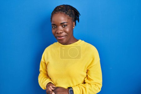Photo for Beautiful black woman standing over blue background with hands together and crossed fingers smiling relaxed and cheerful. success and optimistic - Royalty Free Image