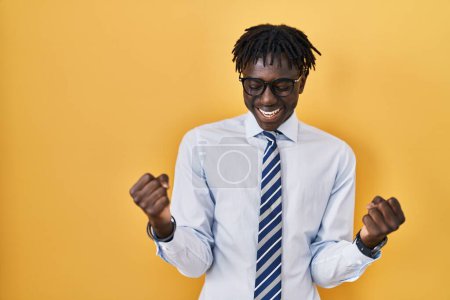 Téléchargez les photos : African man with dreadlocks standing over yellow background very happy and excited doing winner gesture with arms raised, smiling and screaming for success. celebration concept. - en image libre de droit