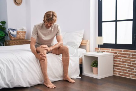 Téléchargez les photos : Jeune homme souffrant d'une blessure au genou assis sur le lit dans la chambre - en image libre de droit
