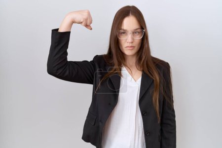 Téléchargez les photos : Belle femme brune portant une veste d'affaires et des lunettes personne forte montrant muscle du bras, confiant et fier de la puissance - en image libre de droit