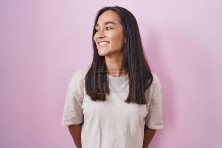 Photo for Young hispanic woman standing over pink background looking away to side with smile on face, natural expression. laughing confident. - Royalty Free Image