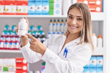 Photo for Young caucasian woman pharmacist smiling confident holding pills bottle at pharmacy - Royalty Free Image
