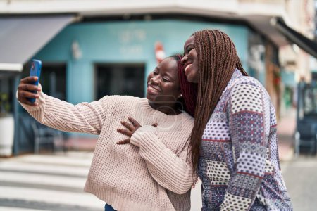 Foto de Afro-americanas amigas sonriendo confiadas hacen selfie por teléfono inteligente en la calle - Imagen libre de derechos