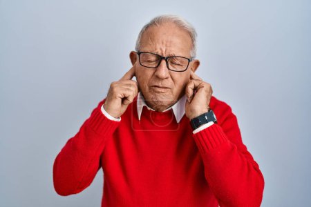 Foto de Hombre mayor con el pelo gris de pie sobre el fondo aislado cubriendo las orejas con los dedos con expresión molesta por el ruido de la música fuerte. concepto de sordo. - Imagen libre de derechos