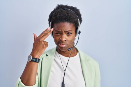Foto de Mujer afroamericana con auriculares de agente de centro de llamadas disparando y matándose apuntando de la mano y los dedos a la cabeza como arma, gesto suicida. - Imagen libre de derechos