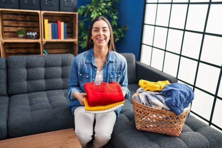 Photo for Hispanic woman holding folded laundry after ironing smiling and laughing hard out loud because funny crazy joke. - Royalty Free Image