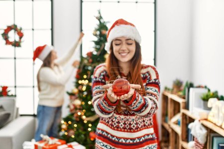 Foto de Mujer pareja sosteniendo bola de Navidad decorando árbol de Navidad en casa - Imagen libre de derechos