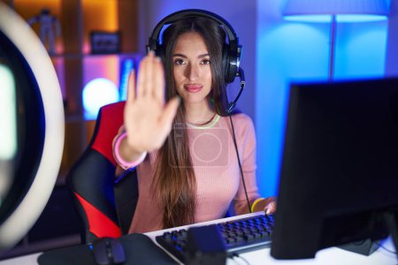 Téléchargez les photos : Jeune femme hispanique jouant à des jeux vidéo faire arrêter de chanter avec la paume de la main. expression d'avertissement avec geste négatif et sérieux sur le visage. - en image libre de droit