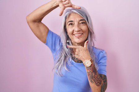 Photo for Middle age woman with tattoos standing over pink background smiling making frame with hands and fingers with happy face. creativity and photography concept. - Royalty Free Image