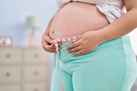 Téléchargez les photos : Jeune femme enceinte mesurant le ventre à la maison - en image libre de droit