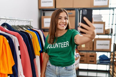 Téléchargez les photos : Jeune femme hispanique portant un uniforme bénévole faisant du selfie par le smartphone au centre de charité - en image libre de droit