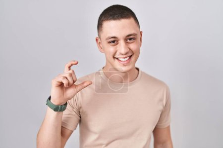 Photo for Young man standing over isolated background smiling and confident gesturing with hand doing small size sign with fingers looking and the camera. measure concept. - Royalty Free Image