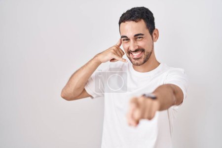 Téléchargez les photos : Handsome hispanic man standing over white background smiling doing talking on the telephone gesture and pointing to you. call me. - en image libre de droit
