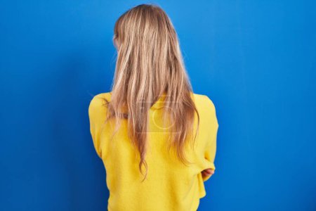 Photo for Young caucasian woman standing over blue background standing backwards looking away with crossed arms - Royalty Free Image
