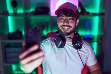 Photo for Young hispanic man streamer using computer make selfie by smarpthone at gamin room - Royalty Free Image