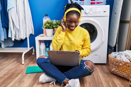 Téléchargez les photos : African american woman listening to music waiting for washing machine at laundry room - en image libre de droit