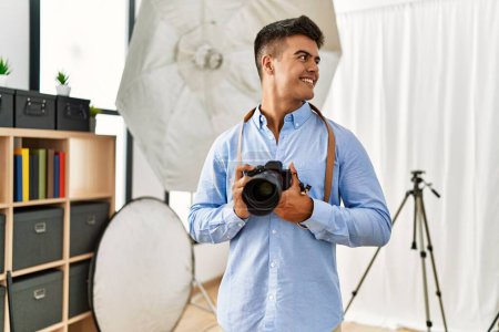 Téléchargez les photos : Jeune homme hispanique photographe utilisant un appareil photo professionnel au studio de photographie - en image libre de droit