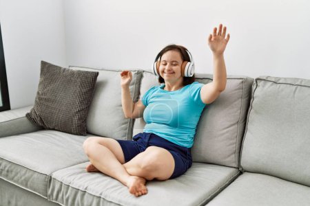 Photo for Brunette woman with down syndrome sitting on the sofa wearing headphones and dancing at the living room - Royalty Free Image