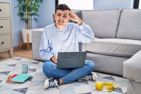 Photo for Non binary person studying using computer laptop sitting on the floor very happy and smiling looking far away with hand over head. searching concept. - Royalty Free Image