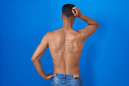 Photo for Young hispanic man standing shirtless over blue background backwards thinking about doubt with hand on head - Royalty Free Image