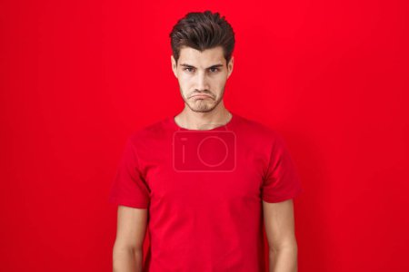 Foto de Young hispanic man standing over red background depressed and worry for distress, crying angry and afraid. sad expression. - Imagen libre de derechos