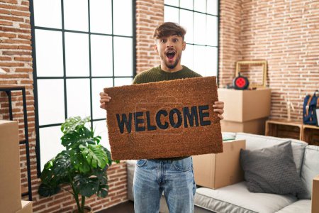 Photo for Arab man with beard holding welcome doormat celebrating crazy and amazed for success with open eyes screaming excited. - Royalty Free Image