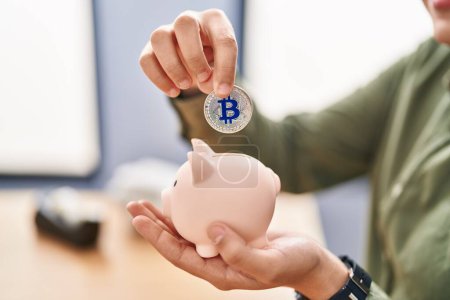 Photo for Young non binary man business worker inserting bitcoin on piggy bank at office - Royalty Free Image