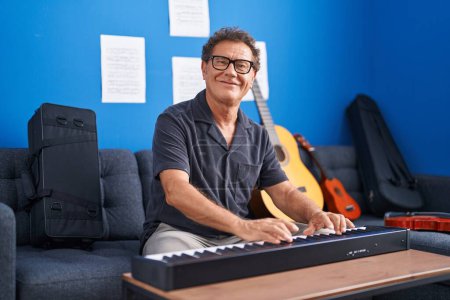 Foto de Middle age man musician smiling confident playing piano at music studio - Imagen libre de derechos