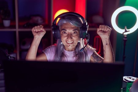 Photo for Middle age grey-haired woman streamer playing video game with winner expression at gaming room - Royalty Free Image