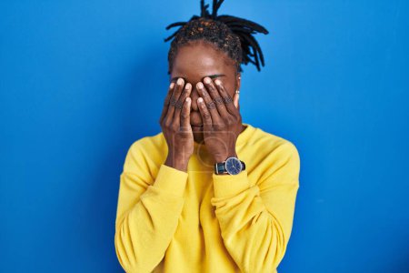 Foto de Beautiful black woman standing over blue background rubbing eyes for fatigue and headache, sleepy and tired expression. vision problem - Imagen libre de derechos