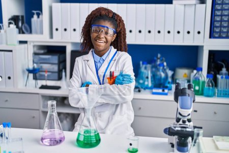 Téléchargez les photos : Femme scientifique afro-américaine souriante confiante debout avec les bras croisés geste au laboratoire - en image libre de droit