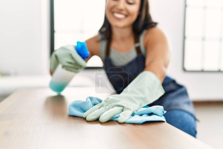 Foto de Joven hermosa mujer hispana sonriendo confiada mesa de limpieza en casa - Imagen libre de derechos