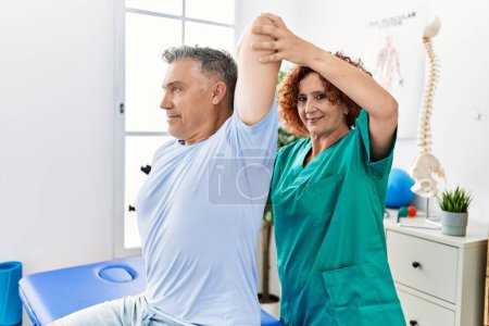 Photo for Middle age man and woman wearing physiotherapy uniform having rehab session stretching arm at physiotherapy clinic - Royalty Free Image