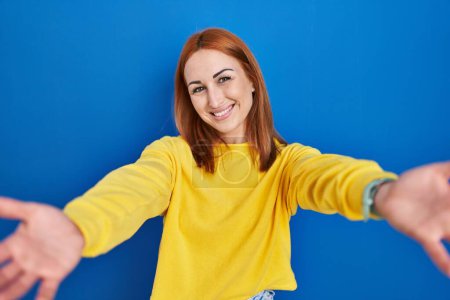 Téléchargez les photos : Young woman standing over blue background looking at the camera smiling with open arms for hug. cheerful expression embracing happiness. - en image libre de droit