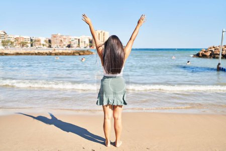 Photo for Young hispanic woman on back view with arms raised up at seaside - Royalty Free Image