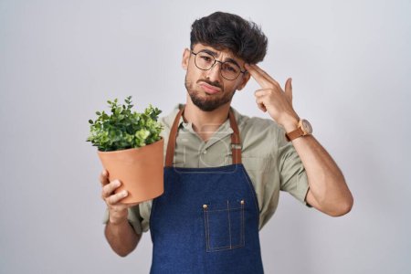 Téléchargez les photos : Arab man with beard holding green plant pot shooting and killing oneself pointing hand and fingers to head like gun, suicide gesture. - en image libre de droit
