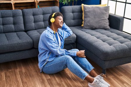 Téléchargez les photos : Femme afro-américaine écoutant de la musique assise sur le sol à la maison - en image libre de droit