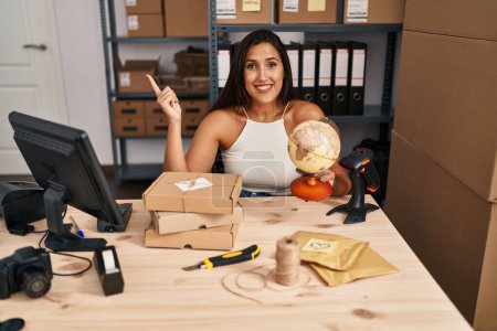 Foto de Young hispanic woman working at small business ecommerce worldship smiling happy pointing with hand and finger to the side - Imagen libre de derechos