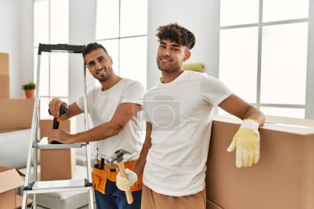 Téléchargez les photos : Deux hommes hispaniques couple souriant maison réparatrice confiante à la nouvelle maison - en image libre de droit