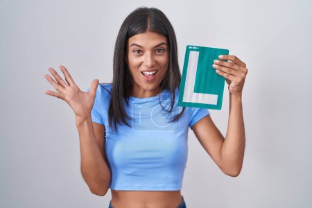 Photo for Brunette young woman holding l sign for new driver celebrating victory with happy smile and winner expression with raised hands - Royalty Free Image