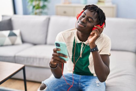 Téléchargez les photos : African american man listening to music sitting on sofa at home - en image libre de droit
