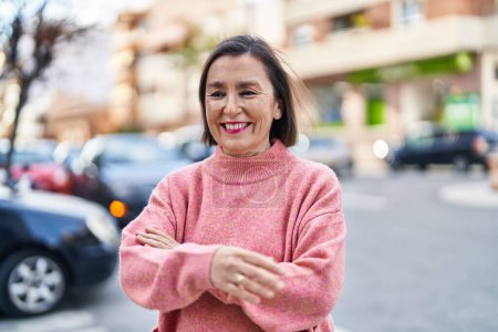 Foto de Mujer de mediana edad sonriendo confiada de pie con los brazos cruzados gesto en la calle - Imagen libre de derechos