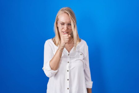 Photo for Young caucasian woman standing over blue background feeling unwell and coughing as symptom for cold or bronchitis. health care concept. - Royalty Free Image