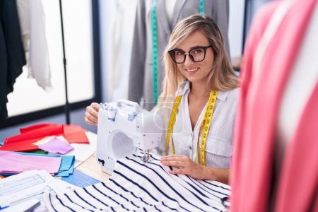 Photo for Young blonde woman tailor smiling confident using sewing machine at tailor shop - Royalty Free Image